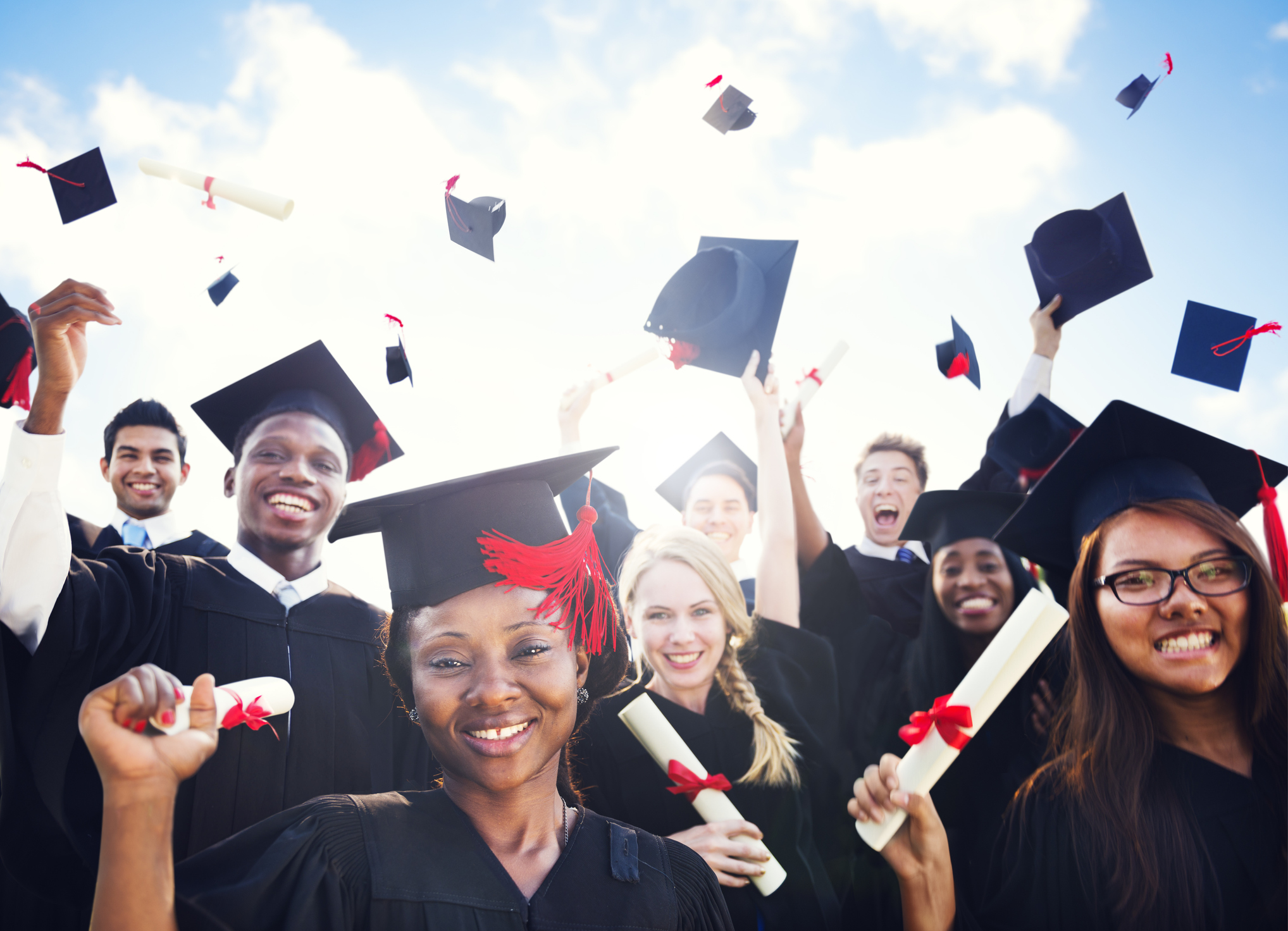 White background with youth in graduation caps in the air and students in black gowns.